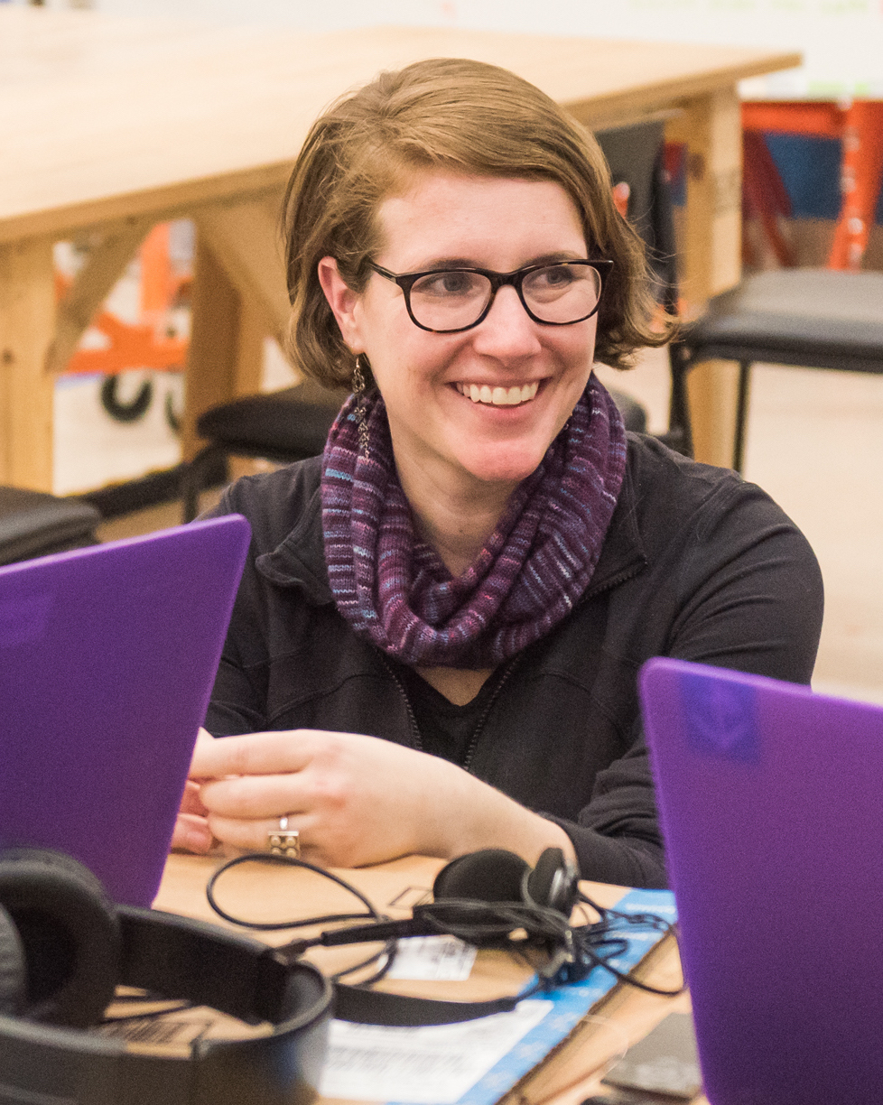 Amy Hurst smiling and sitting between two purple laptops